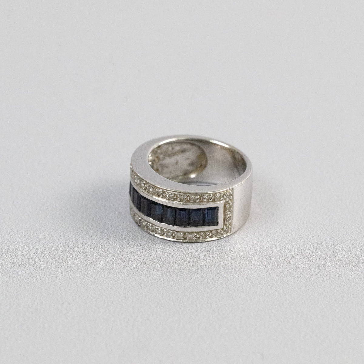 Bague jonc en or blanc avec rangée de saphirs baguettes bleu nuit et entourage de diamants, vue de trois-quarts